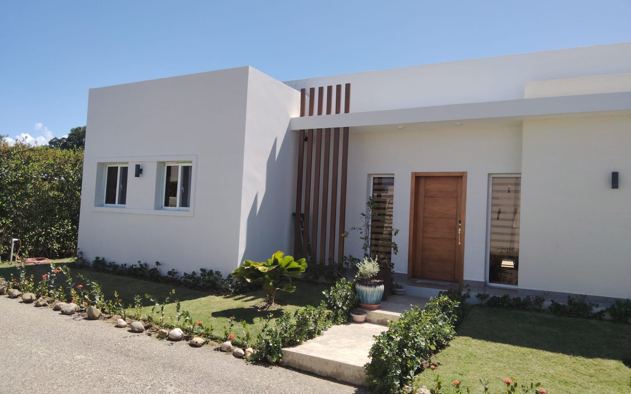 buyDRproperty Modern white house exterior with wooden accents and lush landscaping. Sosua Real Estate