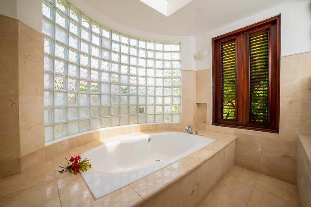 buyDRproperty Luxurious bathroom with a large soaking tub, curved glass block wall, and wooden shutters. Sosua Real Estate