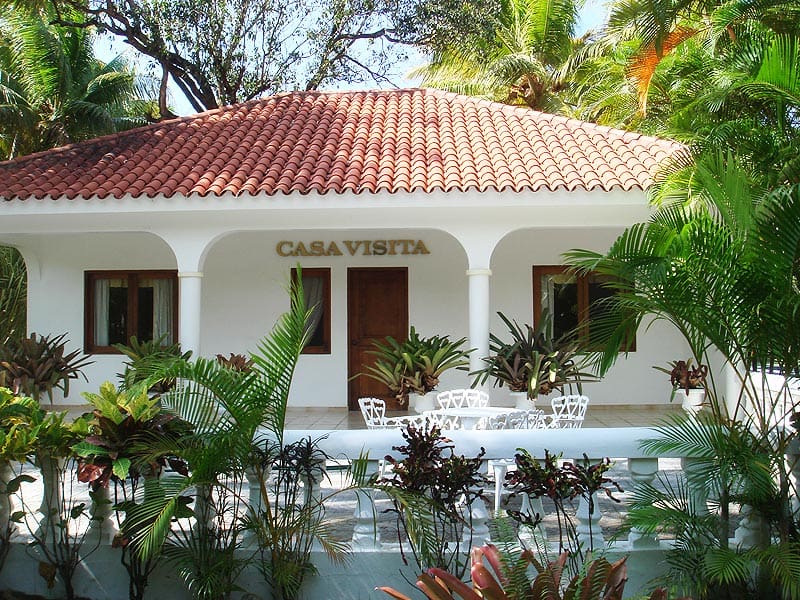 buyDRproperty Casa Visita: white tropical villa with red tile roof and lush greenery. Sosua Real Estate