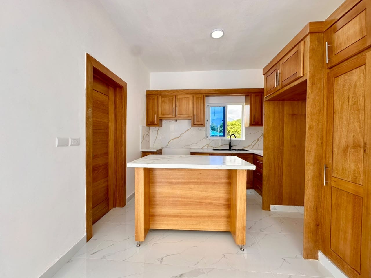 Modern wood kitchen with island, white marble countertops, and stainless steel sink.