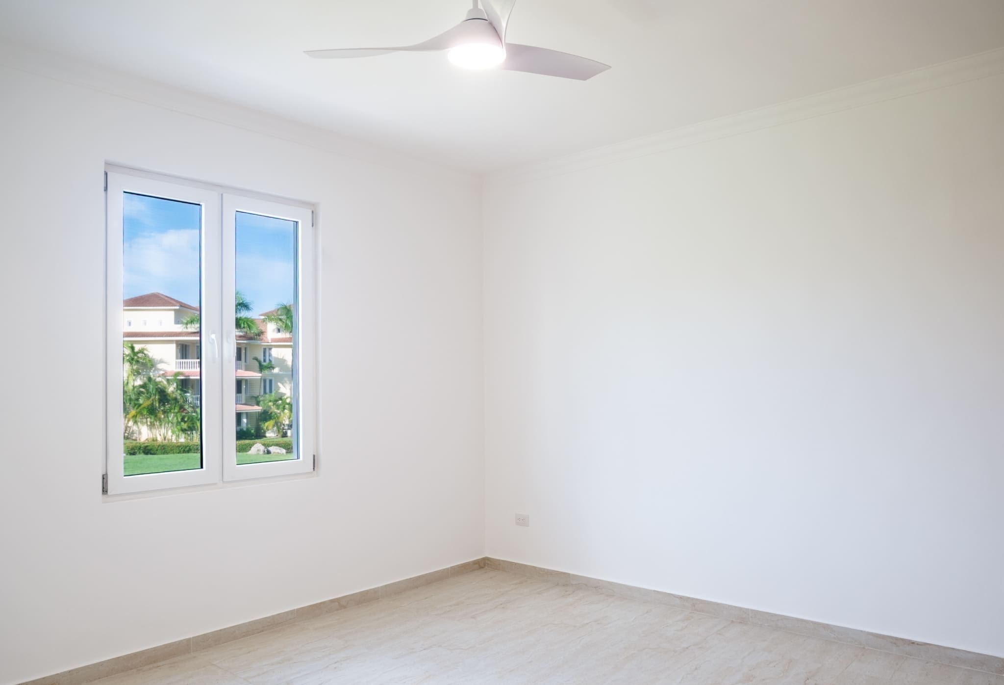 Bright bedroom with ceiling fan, large window and tropical garden views at Hispaniola Beach condo in Sosua