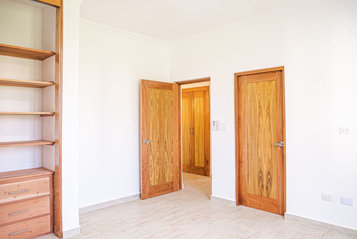 Bright bedroom with built-in wooden shelving, storage drawers and natural wood doors at Hispaniola Beach condo in Sosua