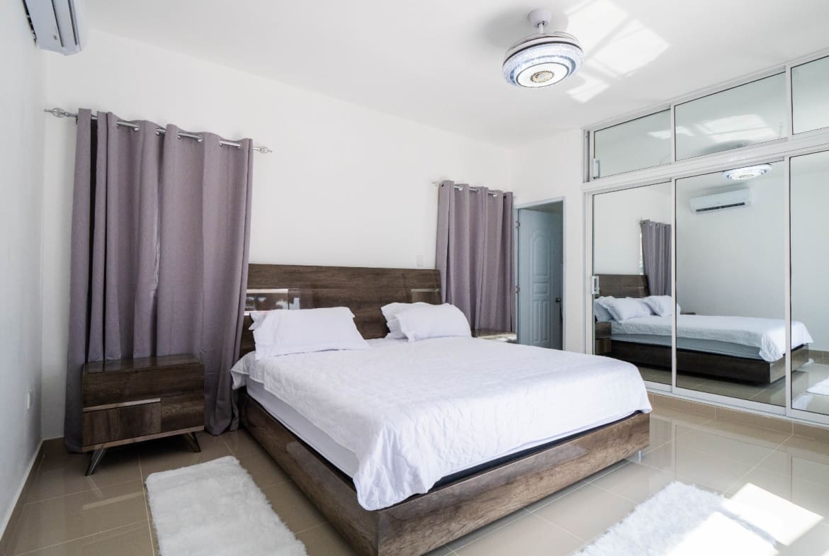 Modern bedroom with white bedding, wooden furniture, and mirrored closet.