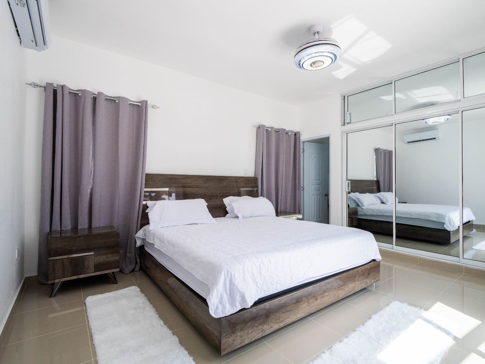 Modern bedroom with white bedding, wooden furniture, and mirrored closet.