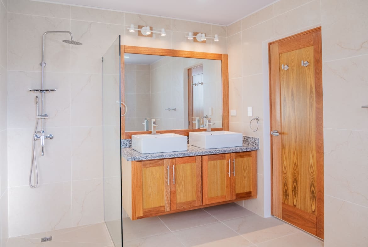 Modern bathroom with double vanity, granite countertop, walk-in shower and wood finishes at Hispaniola Beach condo in Sosua