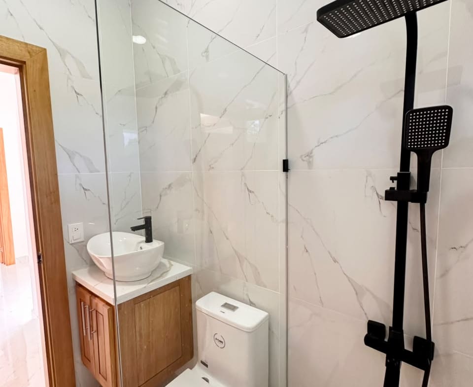 Modern bathroom with black shower fixture, marble tile, and wooden vanity.