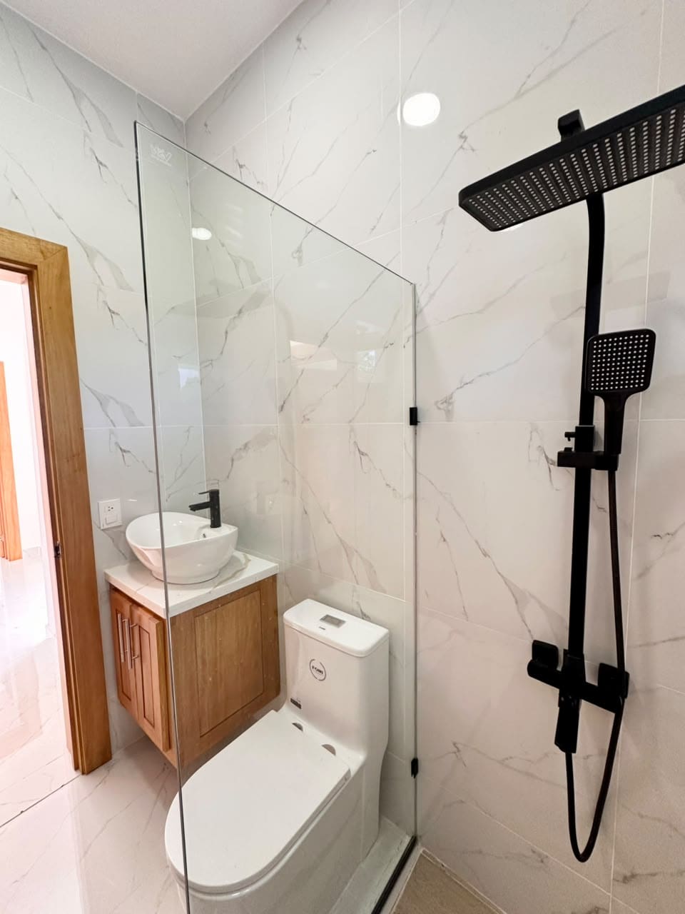 Modern bathroom with black shower fixture, marble tile, and wooden vanity.