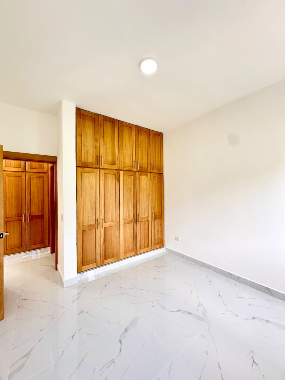 Modern bedroom with large wooden built-in wardrobes and white marble flooring Sosua Real Estate