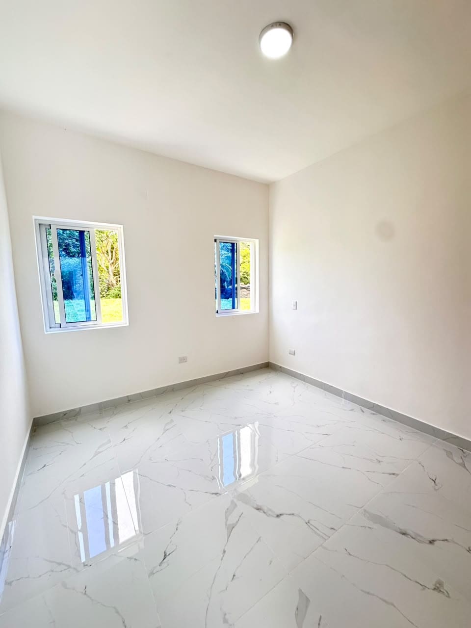 Empty room with white walls, marble tile floors, and blue-tinted windows