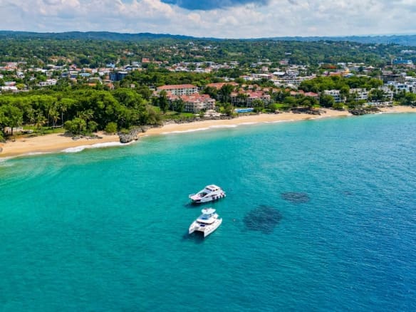 Aerial view of a tropical beach with two yachts in turquoise water and lush green hills.