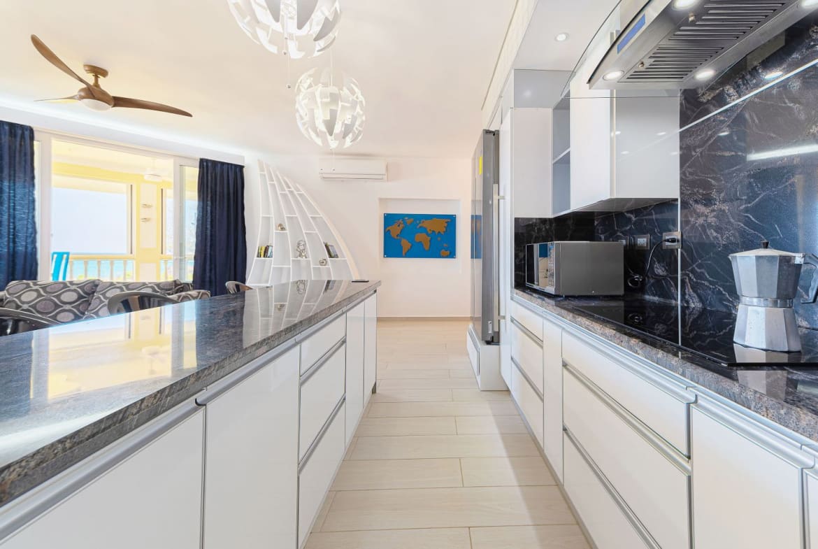 Modern open-plan kitchen with white cabinets, granite countertops, and a world map art piece.