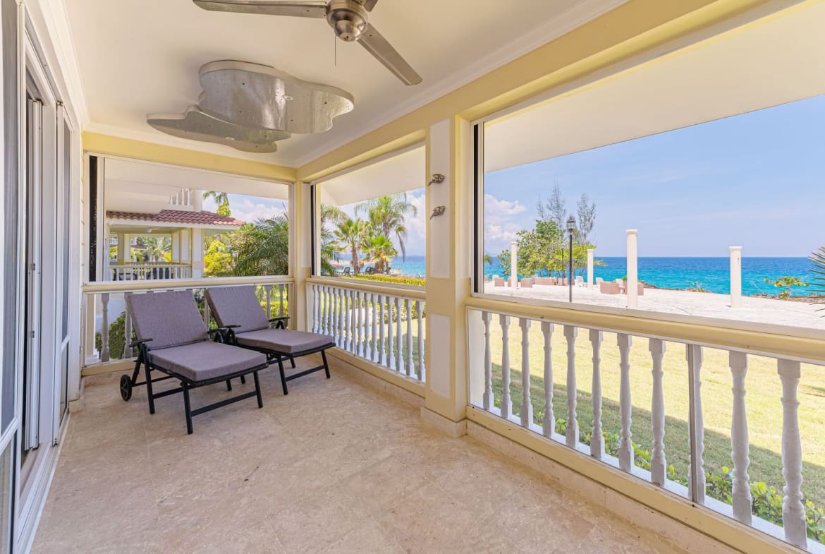 Covered balcony with lounge chairs overlooking a tropical beach and ocean.
