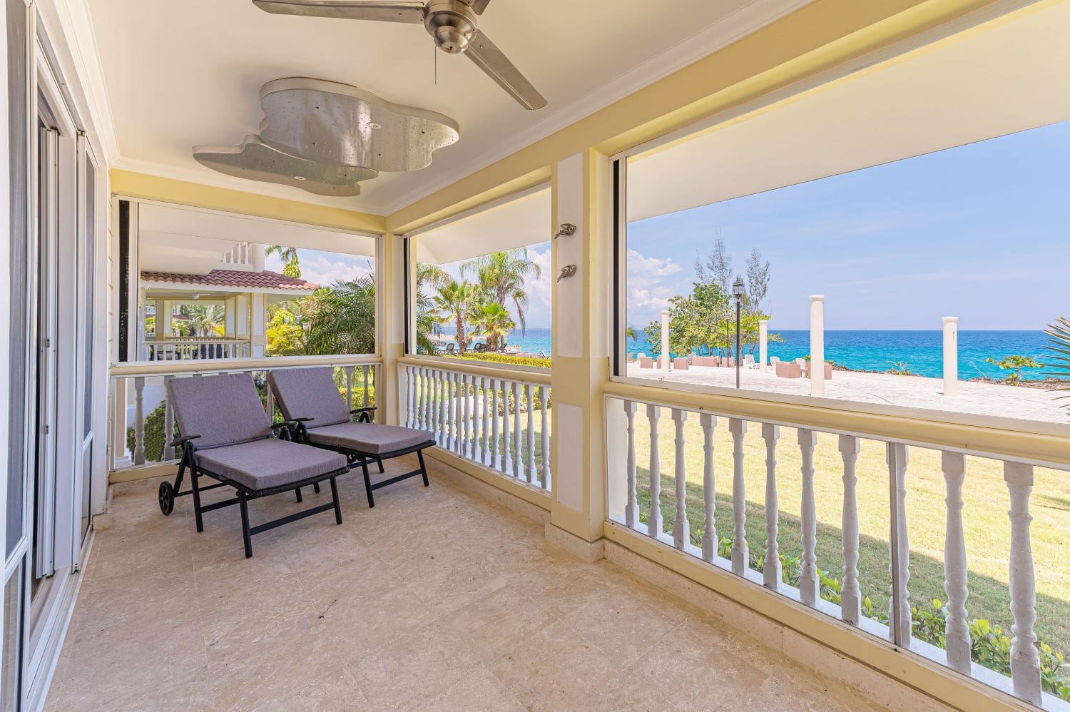 Covered balcony with lounge chairs overlooking a tropical beach and ocean.