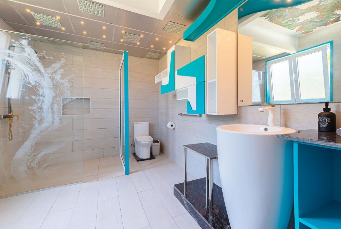 Modern bathroom with turquoise accents, featuring a walk-in shower, toilet, and pedestal sink.