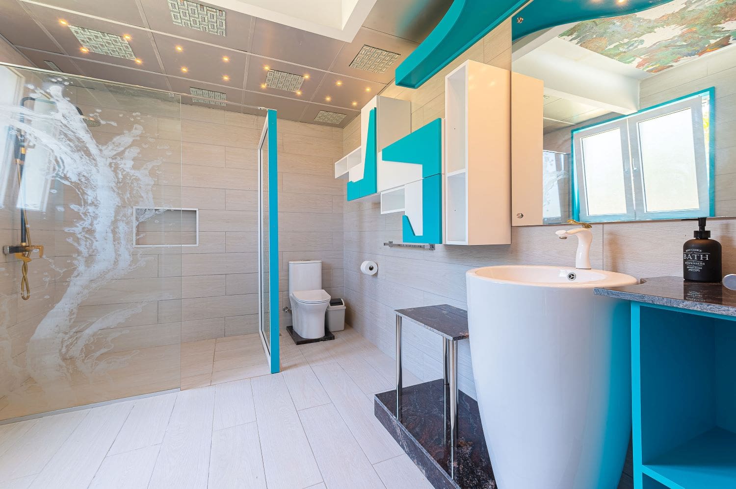 Modern bathroom with turquoise accents, featuring a walk-in shower, toilet, and pedestal sink.
