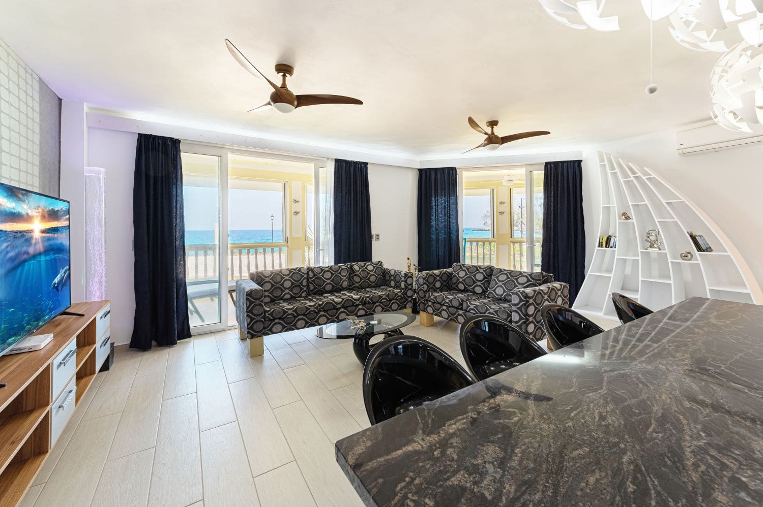 Modern living room with ocean view, featuring patterned sofas, ceiling fans, and a sleek dining area.