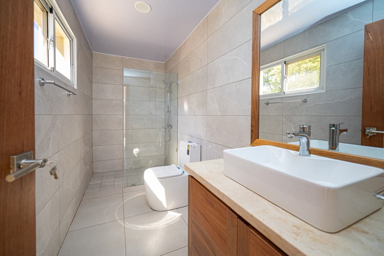 buyDRproperty Modern bathroom with tiled walls, walk-in shower, toilet, and vanity with sink. Sosua Real Estate