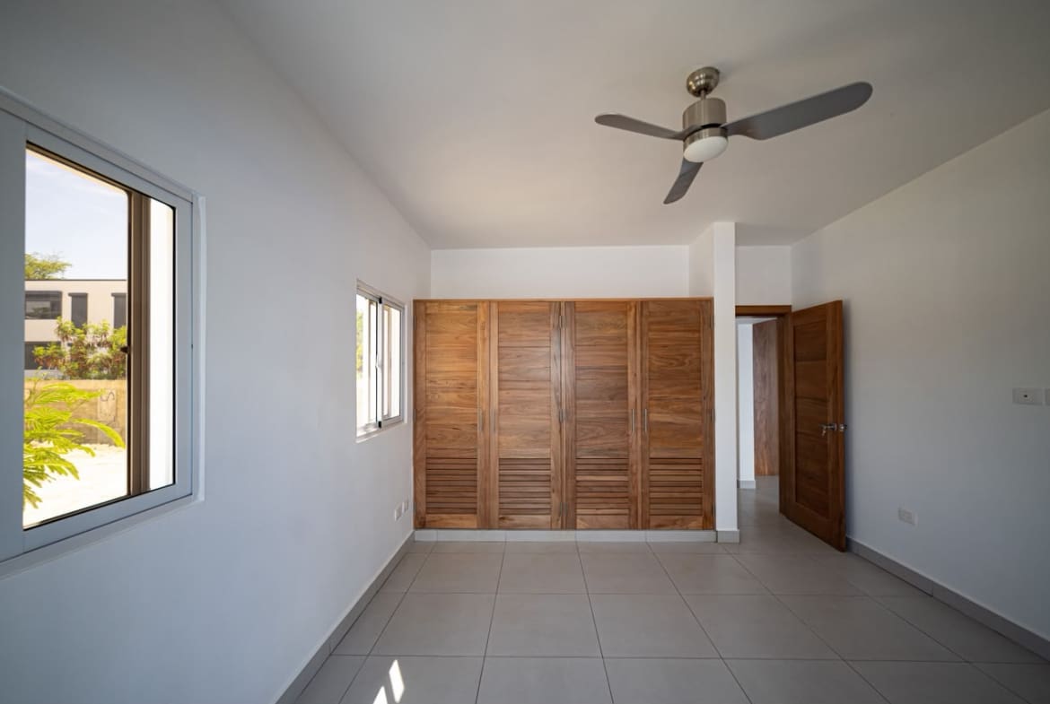 buyDRproperty Spacious bedroom with wooden louvered closet doors, ceiling fan, and window Sosua Real Estate