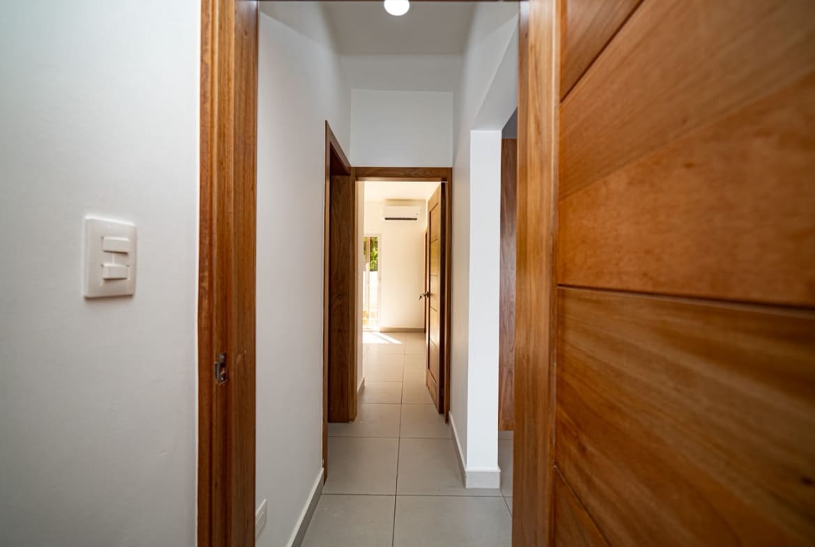 buyDRproperty Interior hallway with wood doors, white walls, and tiled floor leading to a bright room. Sosua Real Estate