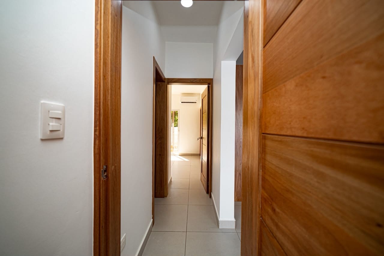 buyDRproperty Interior hallway with wood doors, white walls, and tiled floor leading to a bright room. Sosua Real Estate