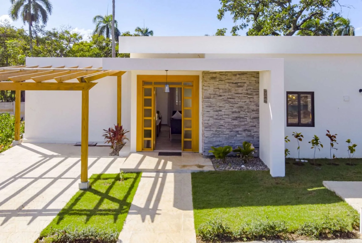 buyDRproperty Modern white house with yellow door, pergola, and tropical landscaping Sosua Real Estate