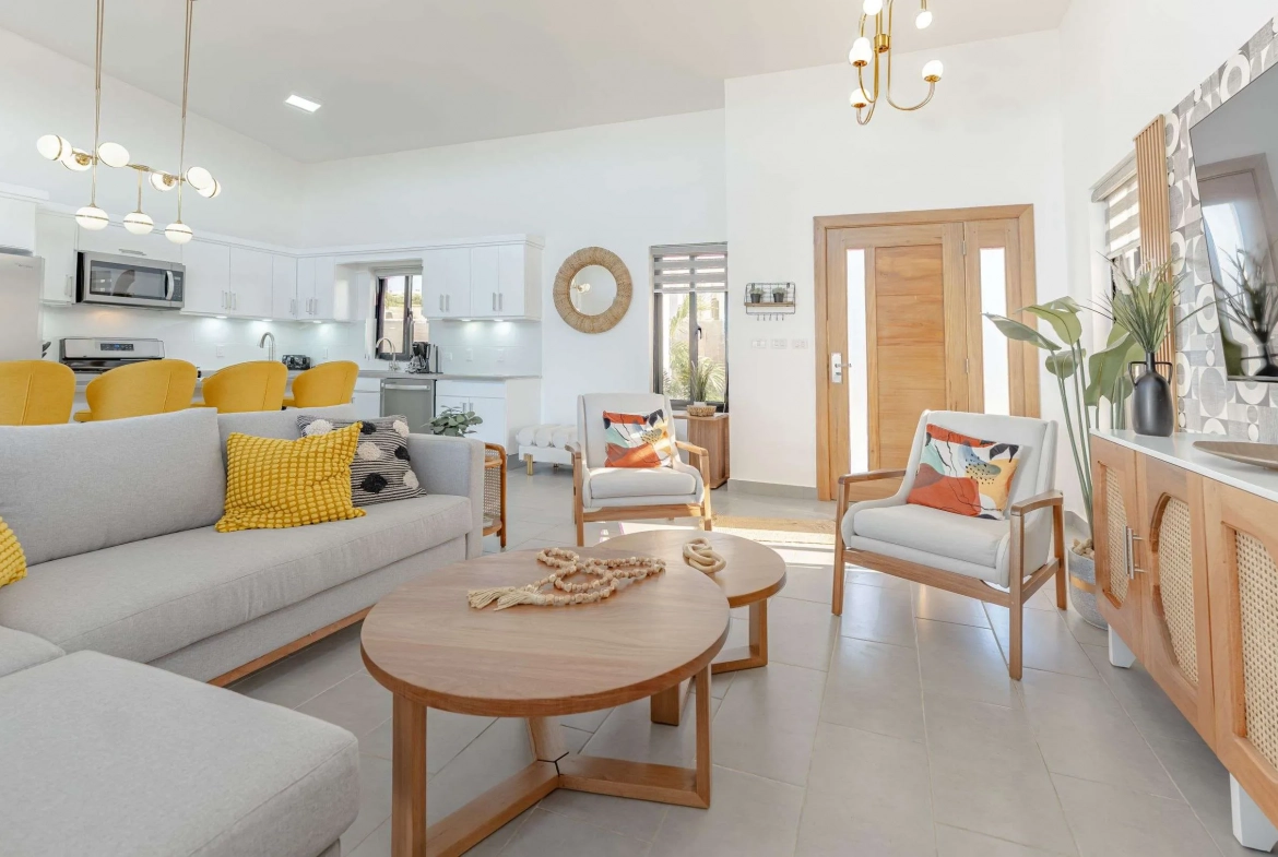 buyDRproperty Modern living room with light grey sectional sofa, wooden coffee table, and white armchairs. Sosua Real Estate