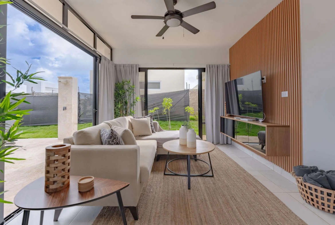 buyDRproperty Modern living room with sectional sofa, TV, and large sliding glass doors opening to a backyard. Sosua Real Estate