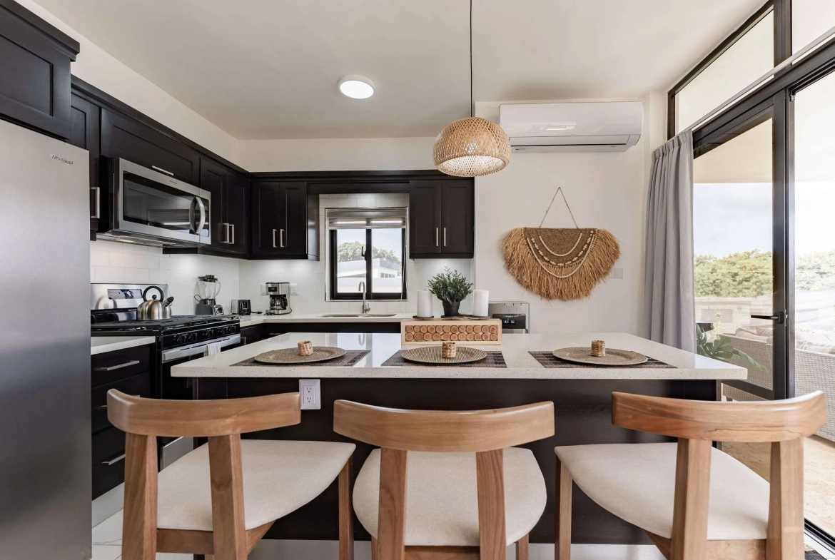 buyDRproperty Modern kitchen island with bar stools, dark cabinets, and stainless steel appliances. Sosua Real Estate