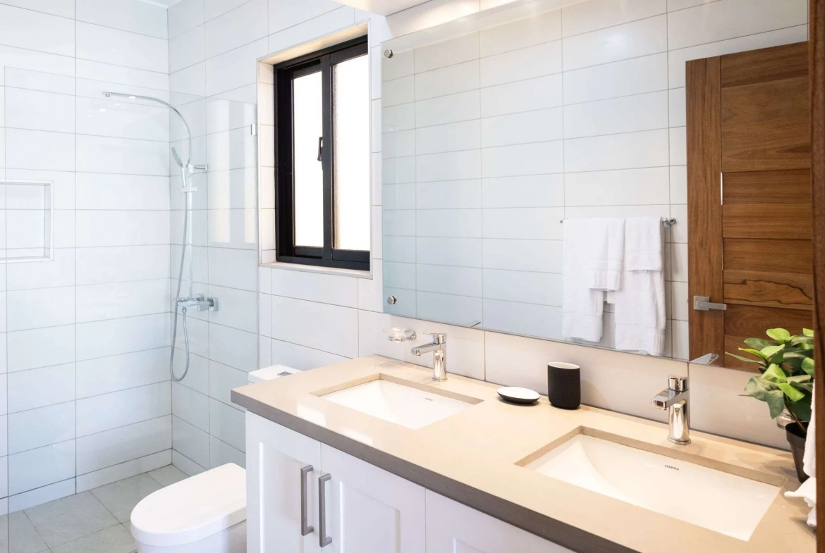 buyDRproperty Modern bathroom with double vanity, white tiled shower, and wooden door. Sosua Real Estate