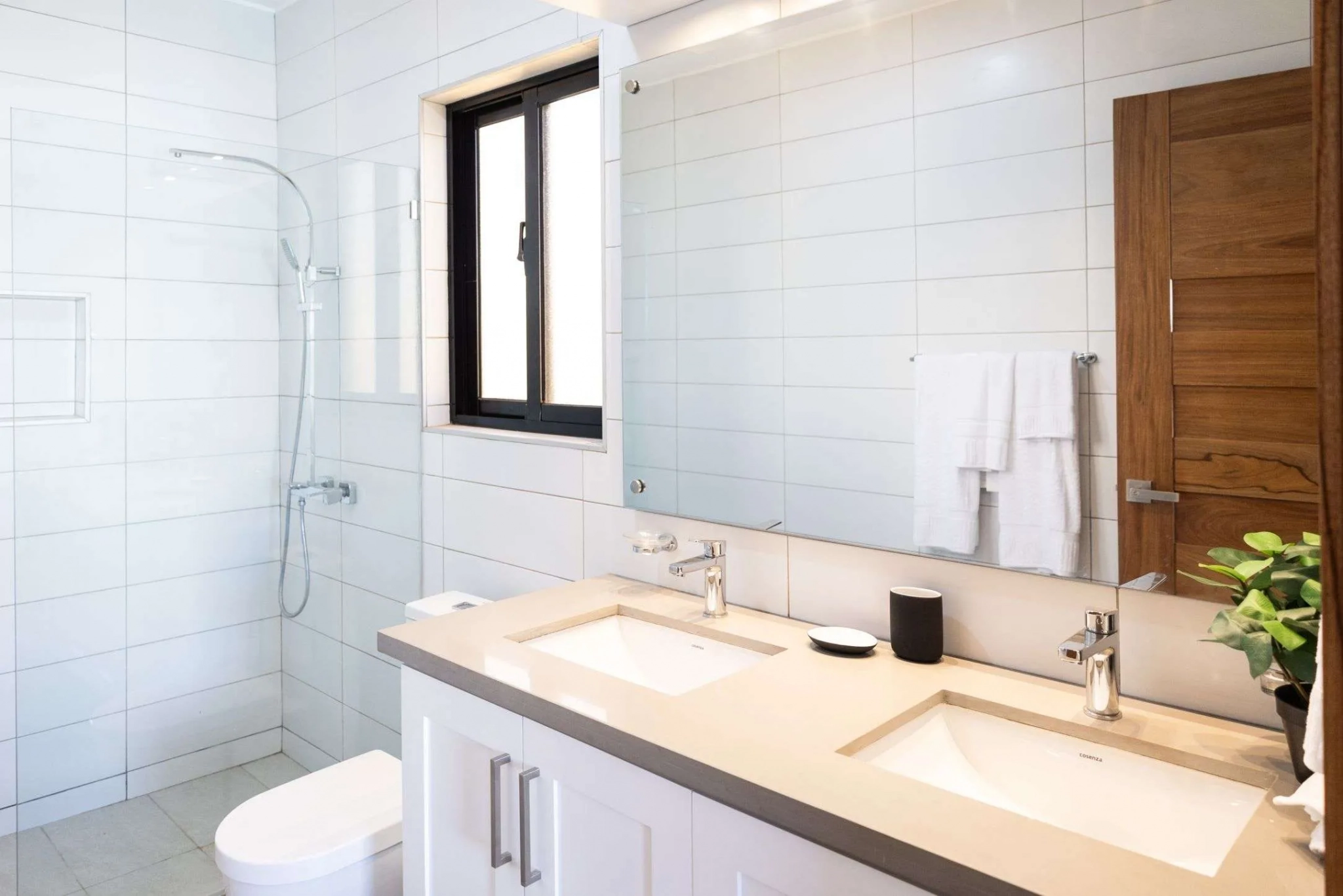 buyDRproperty Modern bathroom with double vanity, white tiled shower, and wooden door. Sosua Real Estate