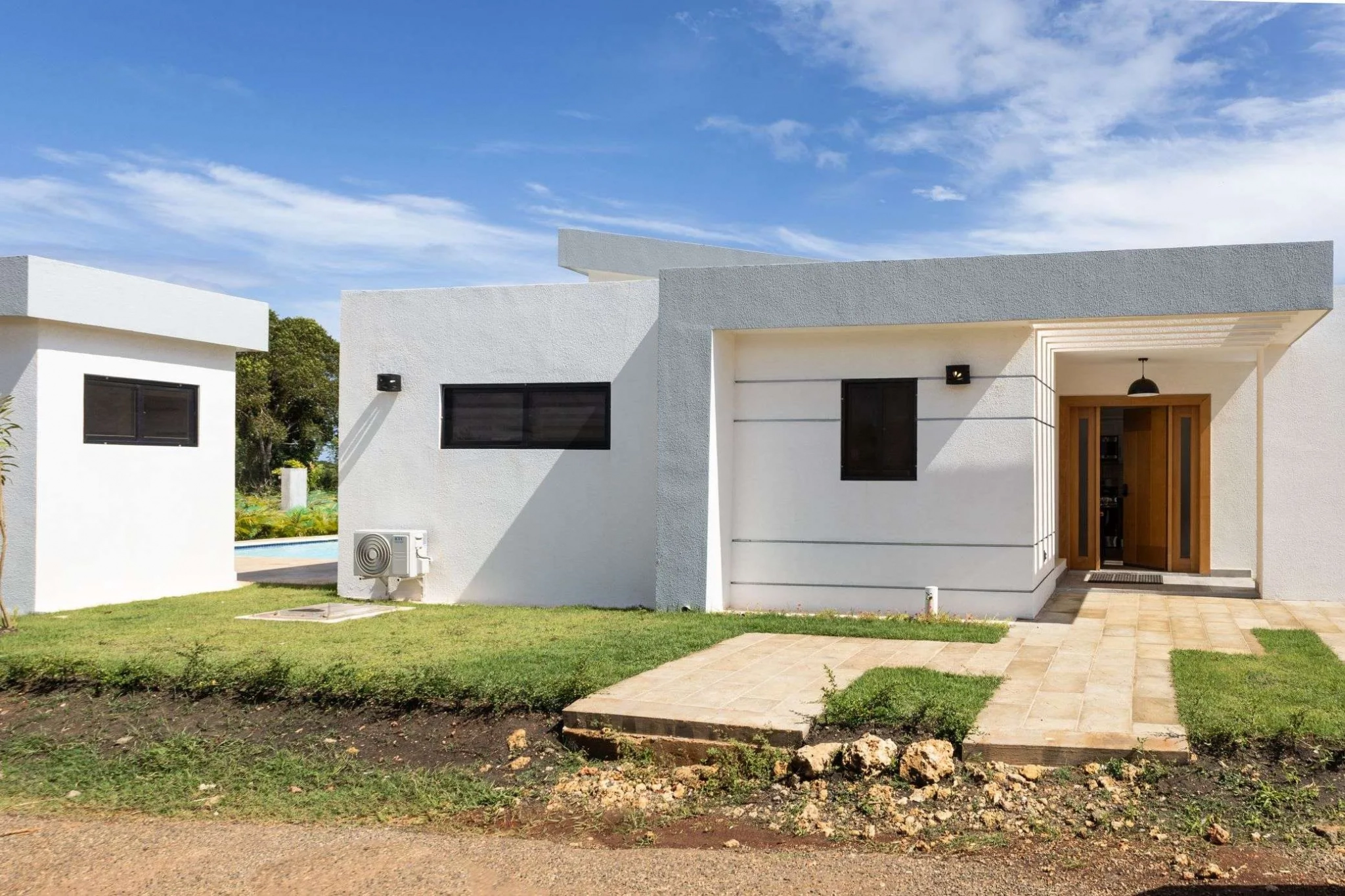 buyDRproperty Modern white house with gray accents and a wooden door, featuring a clean landscape. Sosua Real Estate