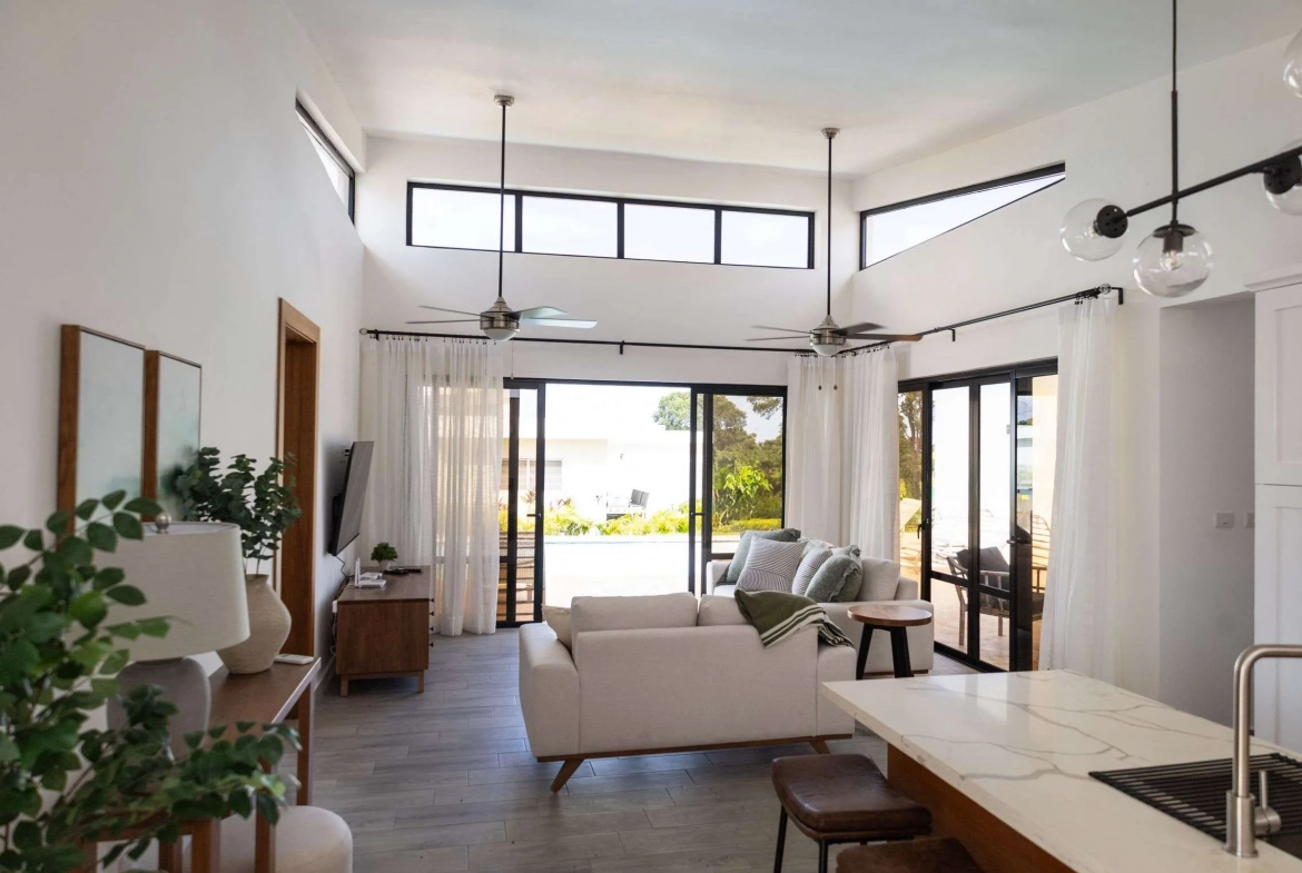 buyDRproperty Modern living room with white sofa, ceiling fans, and large windows overlooking a pool Sosua Real Estate