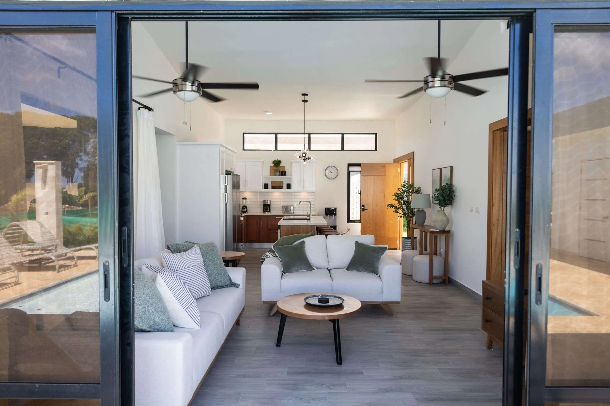 buyDRproperty Modern open-plan living room with white sofas, kitchen, and pool view Sosua Real Estate