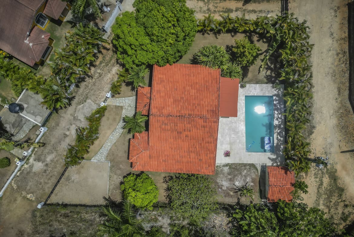 Aerial view of a tropical villa with a red-tiled roof, swimming pool, and lush greenery.