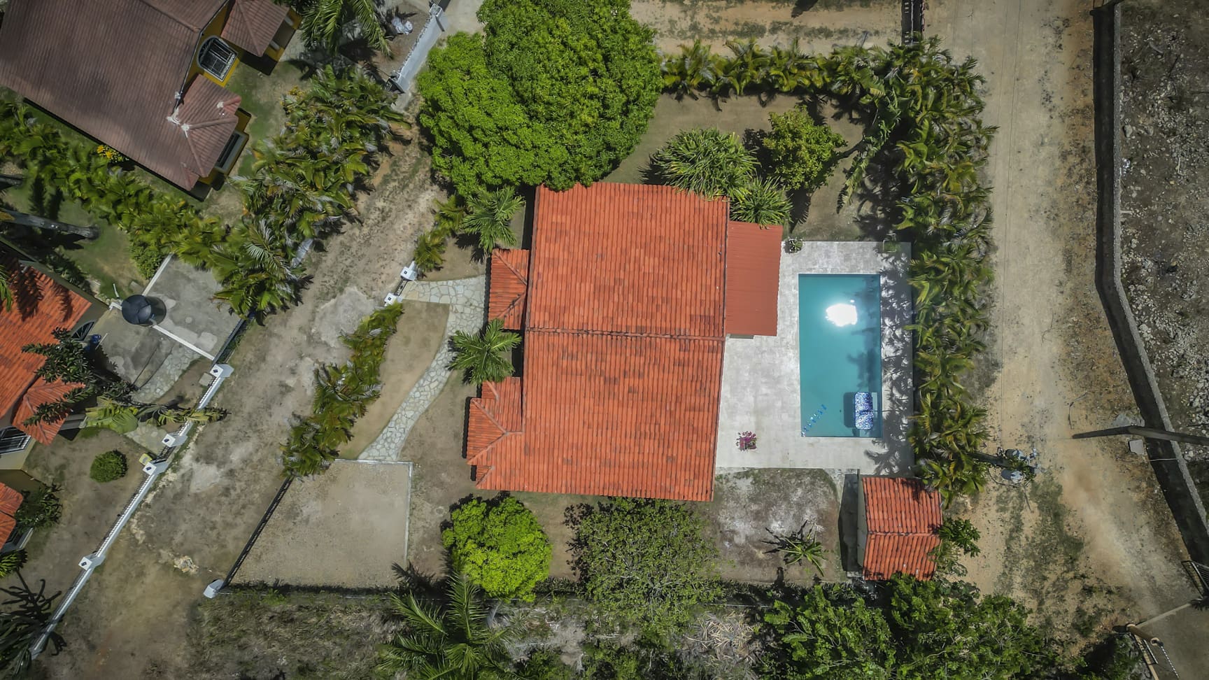Aerial view of a tropical villa with a red-tiled roof, swimming pool, and lush greenery.