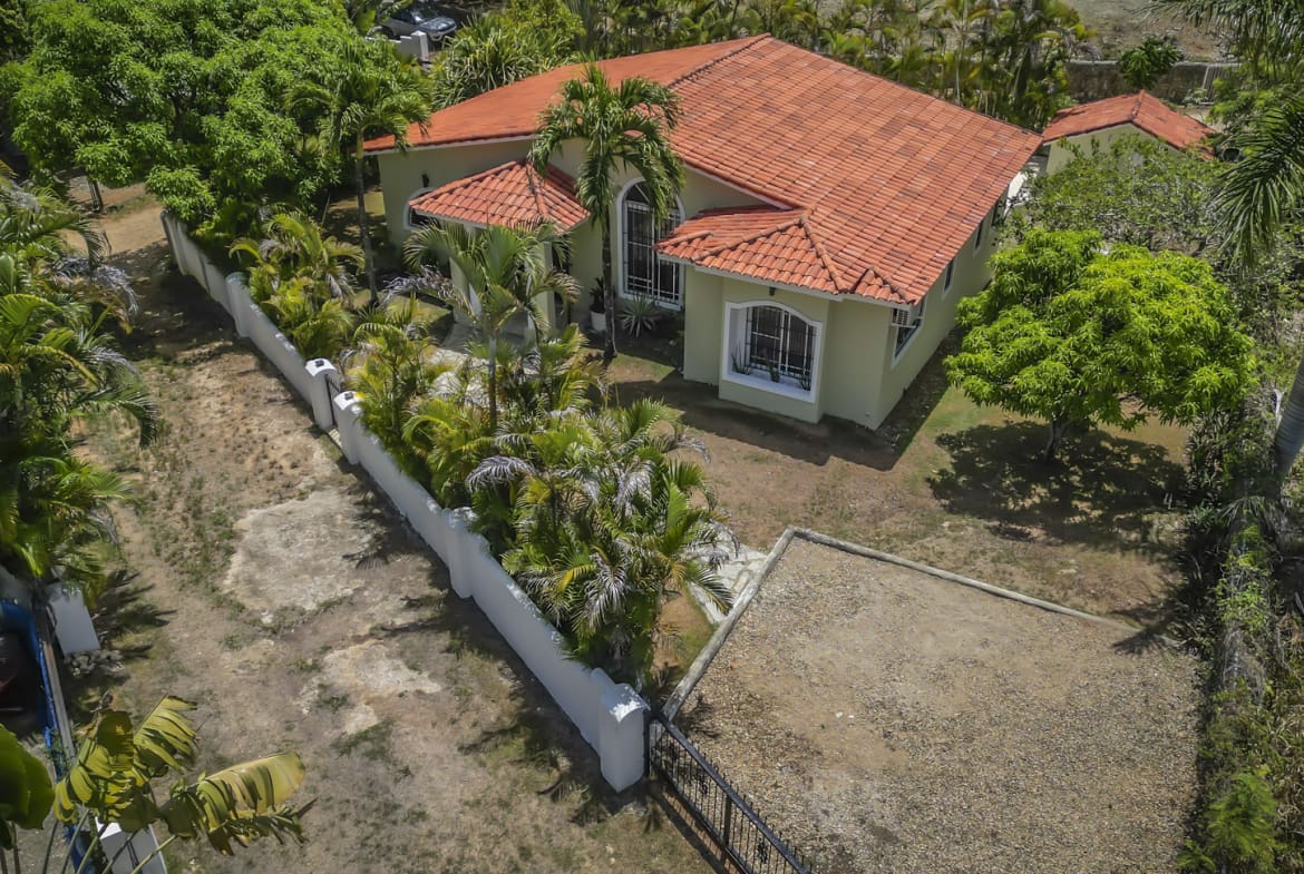 Tropical villa in La Mulata with red tile roof surrounded by lush greenery and palm trees.