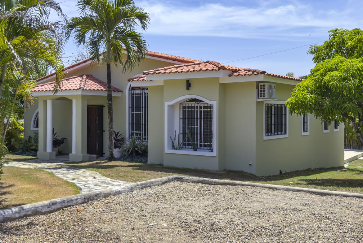 Light green single-story house with red tile roof and palm trees.