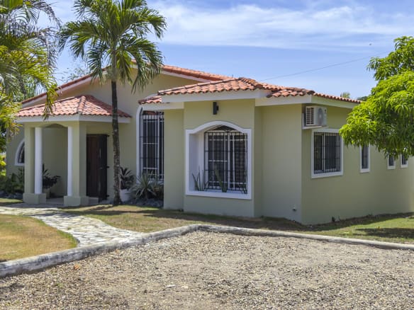 Light green single-story house with red tile roof and palm trees.