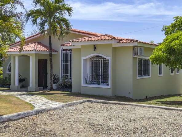 Light green single-story house with red tile roof and palm trees.