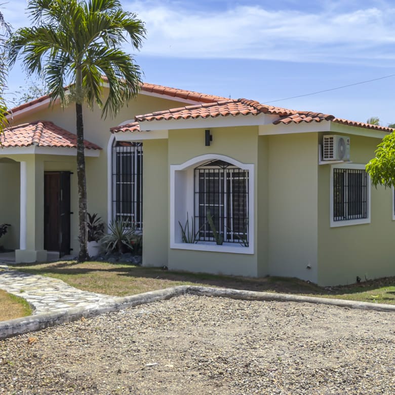 Light green single-story house with red tile roof and palm trees.