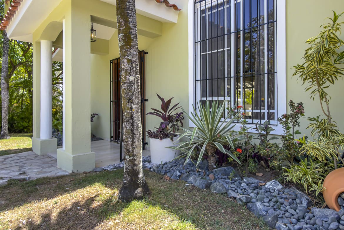 Tropical home exterior with a covered porch, window, and lush plants.
