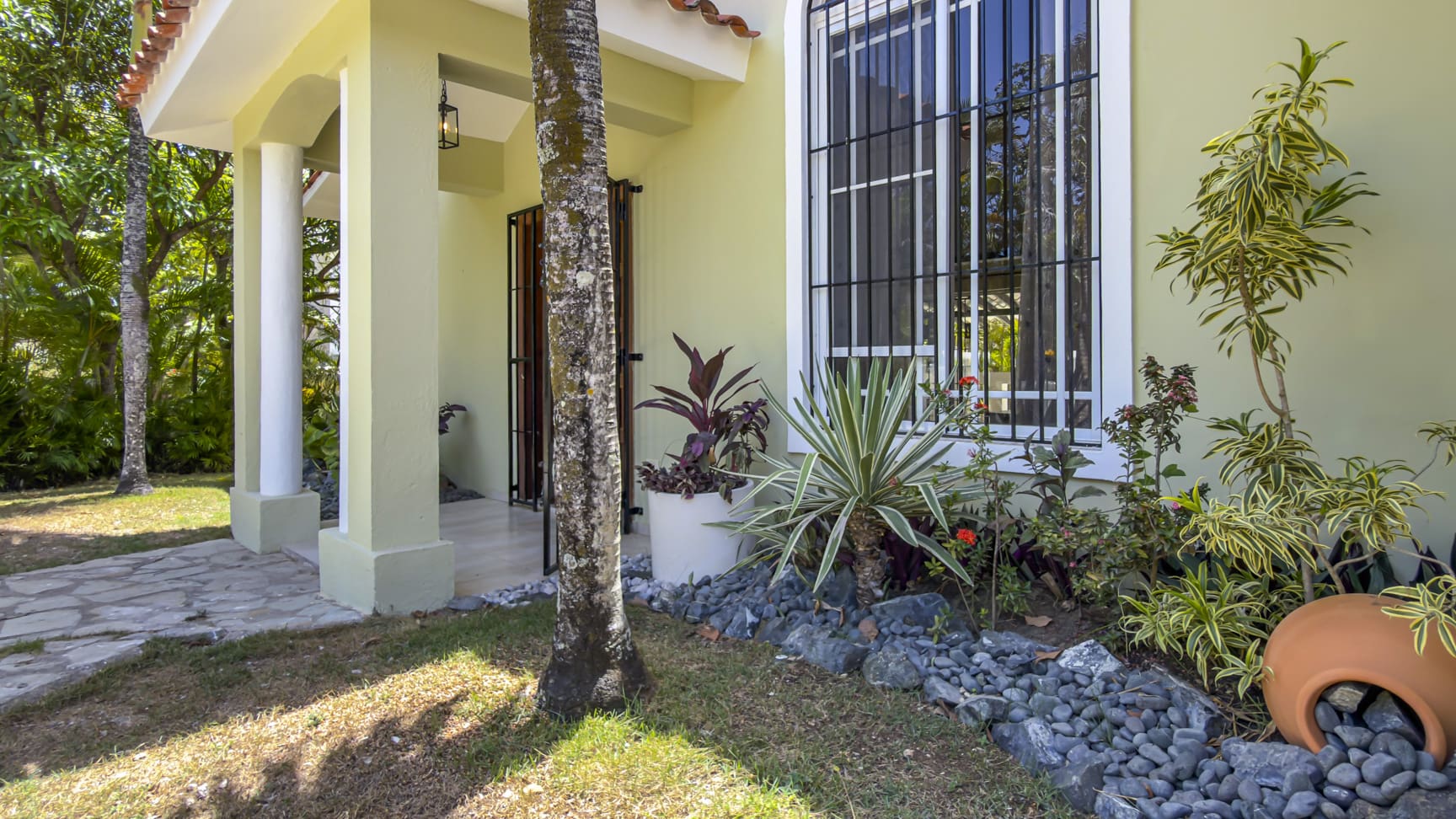 Tropical home exterior with a covered porch, window, and lush plants.