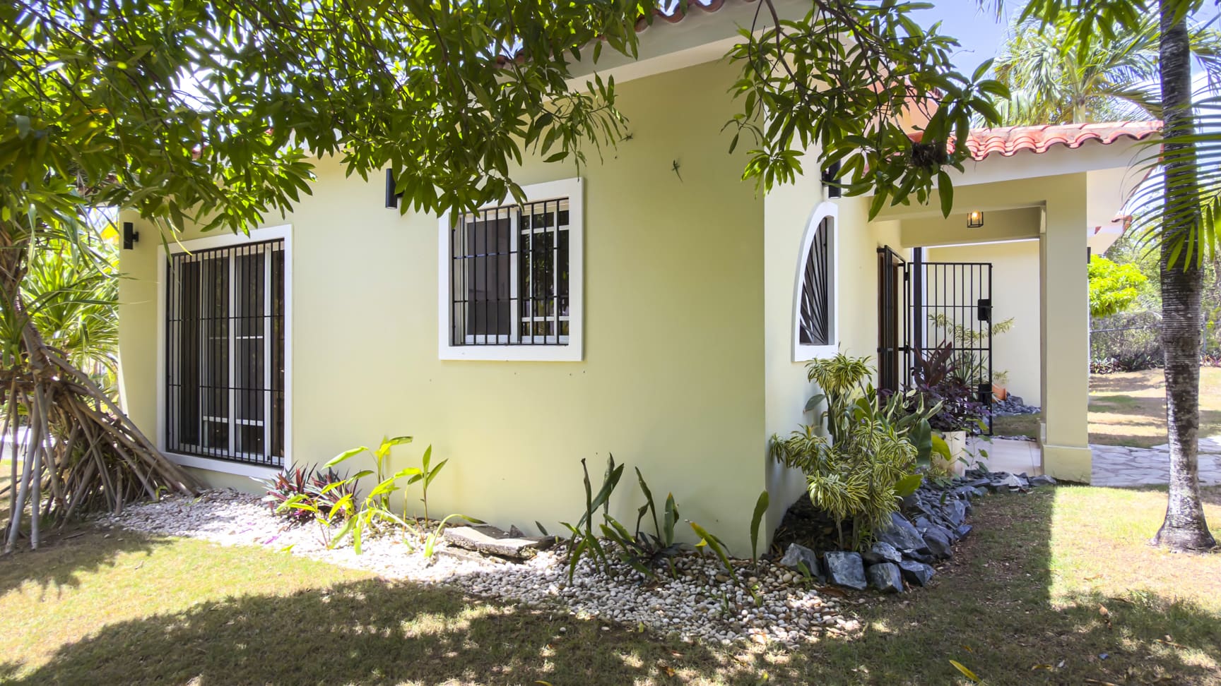 Light green Caribbean villa in Sosua with tiled roof and lush tropical landscaping.