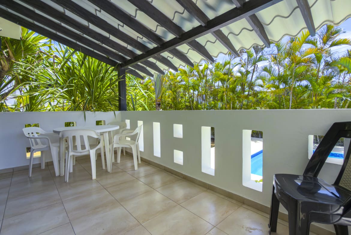 Outdoor patio with white table and chairs, overlooking a tropical pool area.