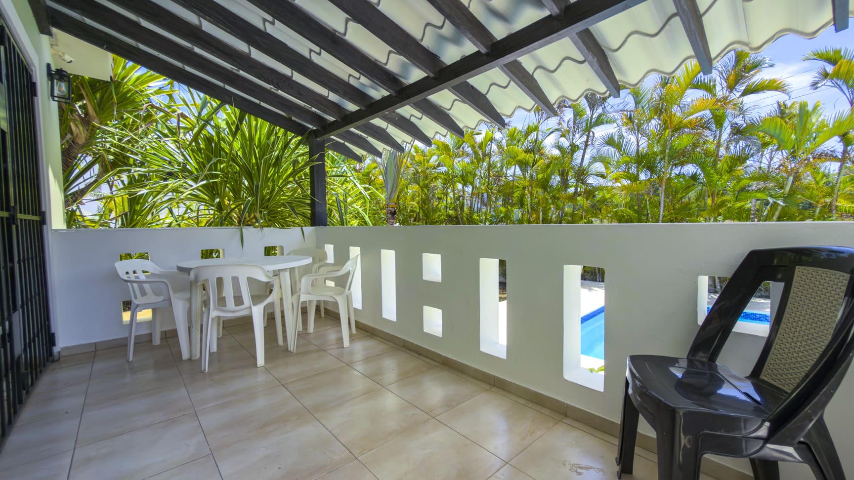 Outdoor patio with white table and chairs, overlooking a tropical pool area.