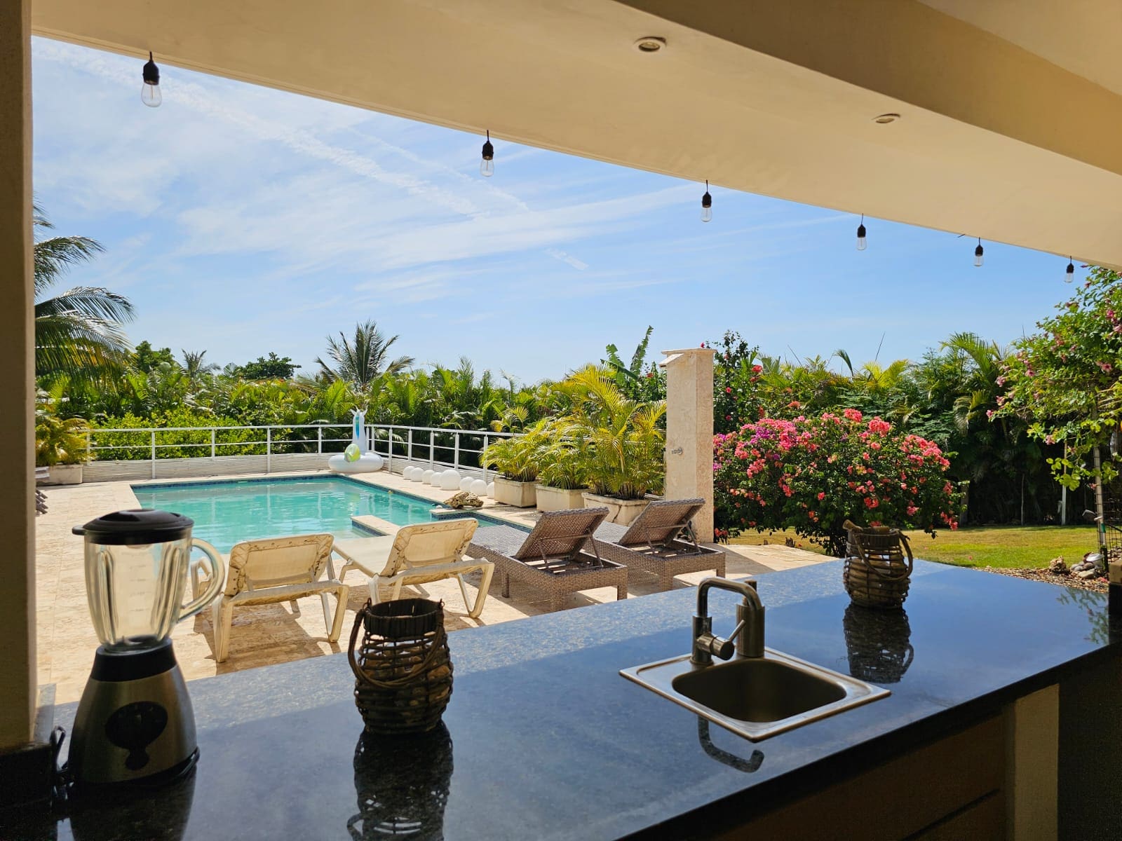 buyDRproperty Outdoor kitchen bar overlooking a tropical pool area with lounge chairs and lush greenery Sosua Real Estate