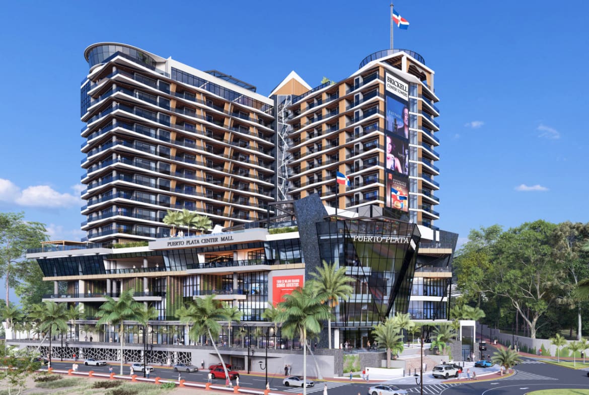 Modern mixed-use shopping complex with two tall towers and a glass atrium, labeled Puerto Plata Center Mall, set against a blue sky with palm trees.