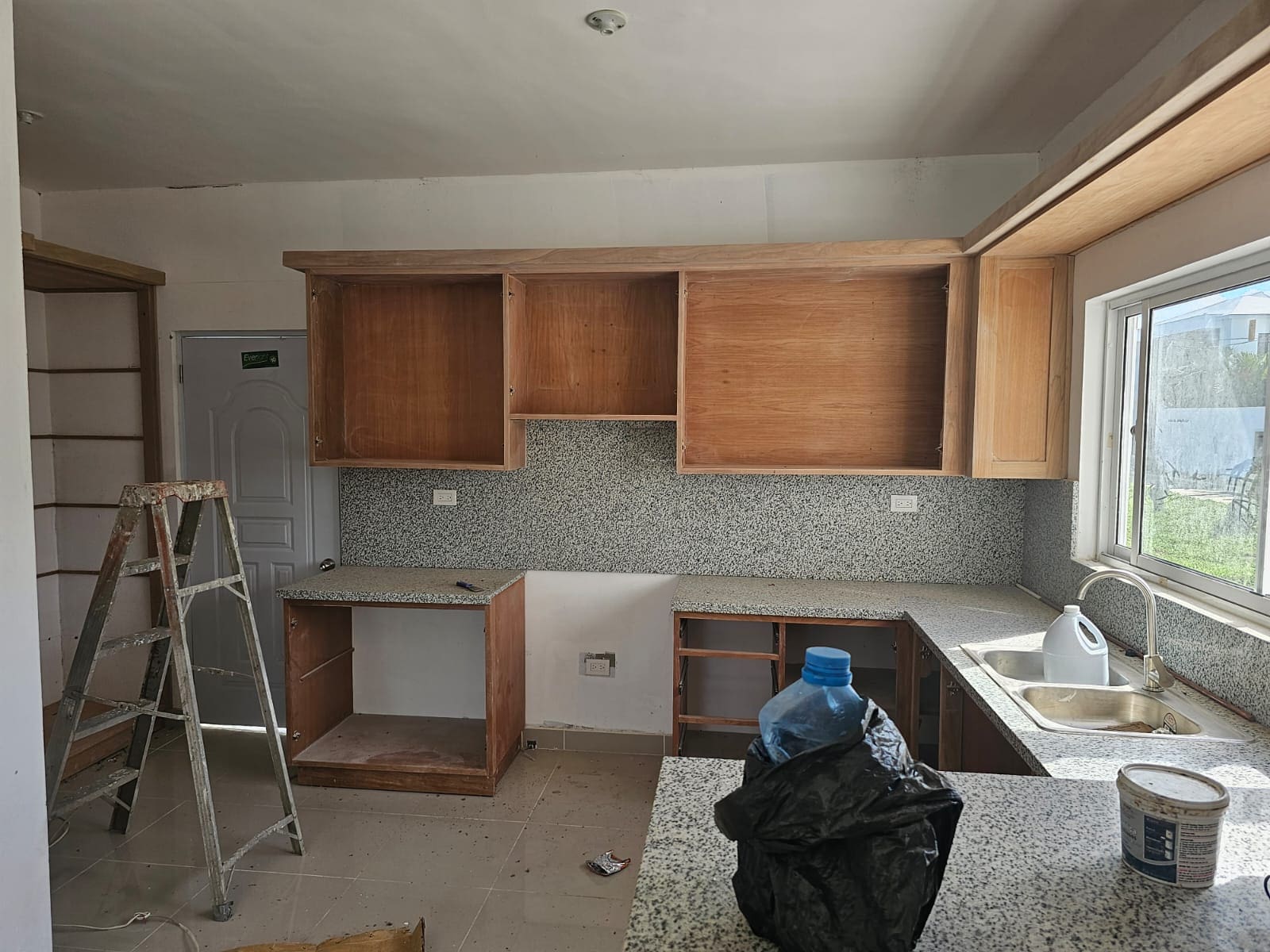 Kitchen renovation: unfinished wooden cabinets, granite countertops, and speckled backsplash.