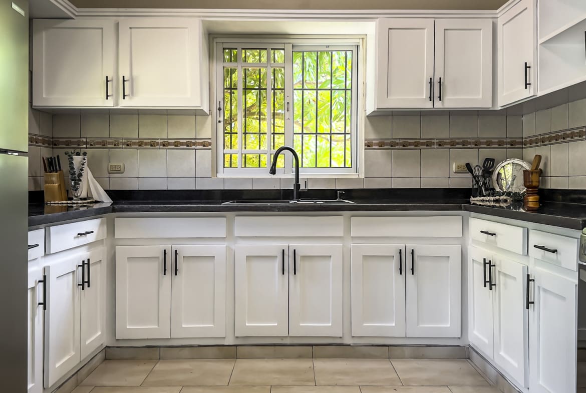 White kitchen cabinets and countertops with a sink and window view.