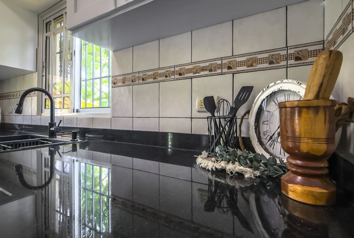Modern kitchen counter with sink, faucet, utensils, clock, and mortar and pestle.